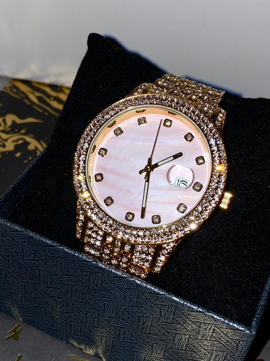Gold-tone women's watch with a diamond-studded bezel, pink mother-of-pearl dial, and date display at the 3 o'clock position. The watch features a shimmering, crystal-encrusted gold band for a glamorous and luxurious look.