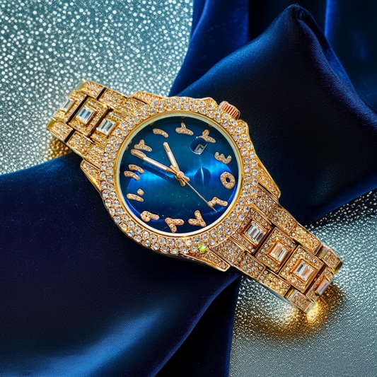 Gold-tone women's watch with diamond-studded bezel, featuring a blue dial with unique, stylized numbers and a date display. The watch has a sparkling, crystal-encrusted band for a glamorous, luxurious look.