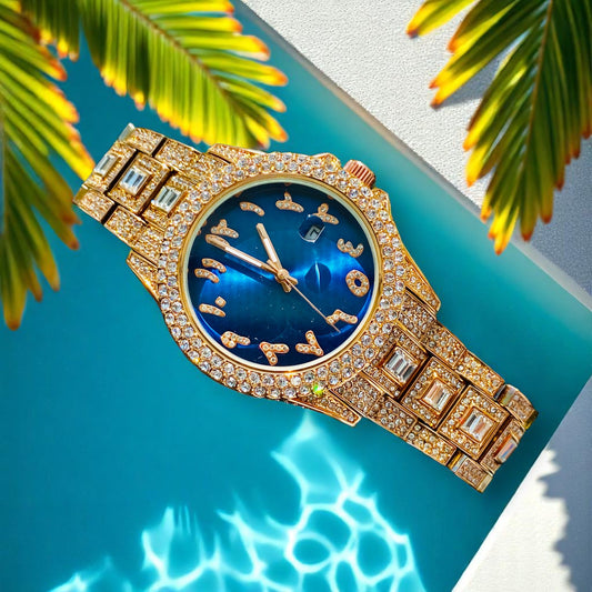 Gold-tone women's watch with diamond-studded bezel, featuring a blue dial with unique, stylized numbers and a date display. The watch has a sparkling, crystal-encrusted band for a glamorous, luxurious look.