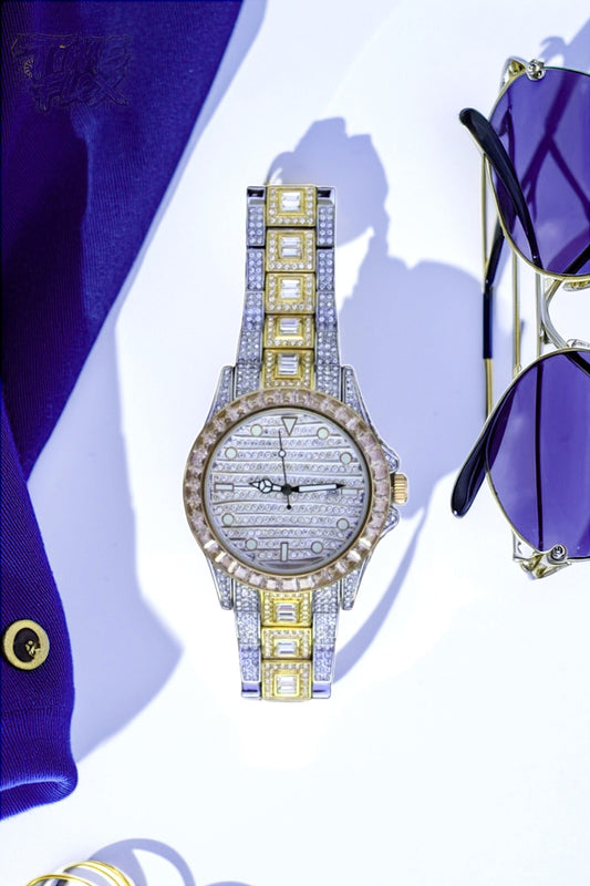 Silver and gold men's women's watch with a diamond-studded bezel and rectangular stone accents on the band. The watch features a sleek white dial with black hands and a date display.