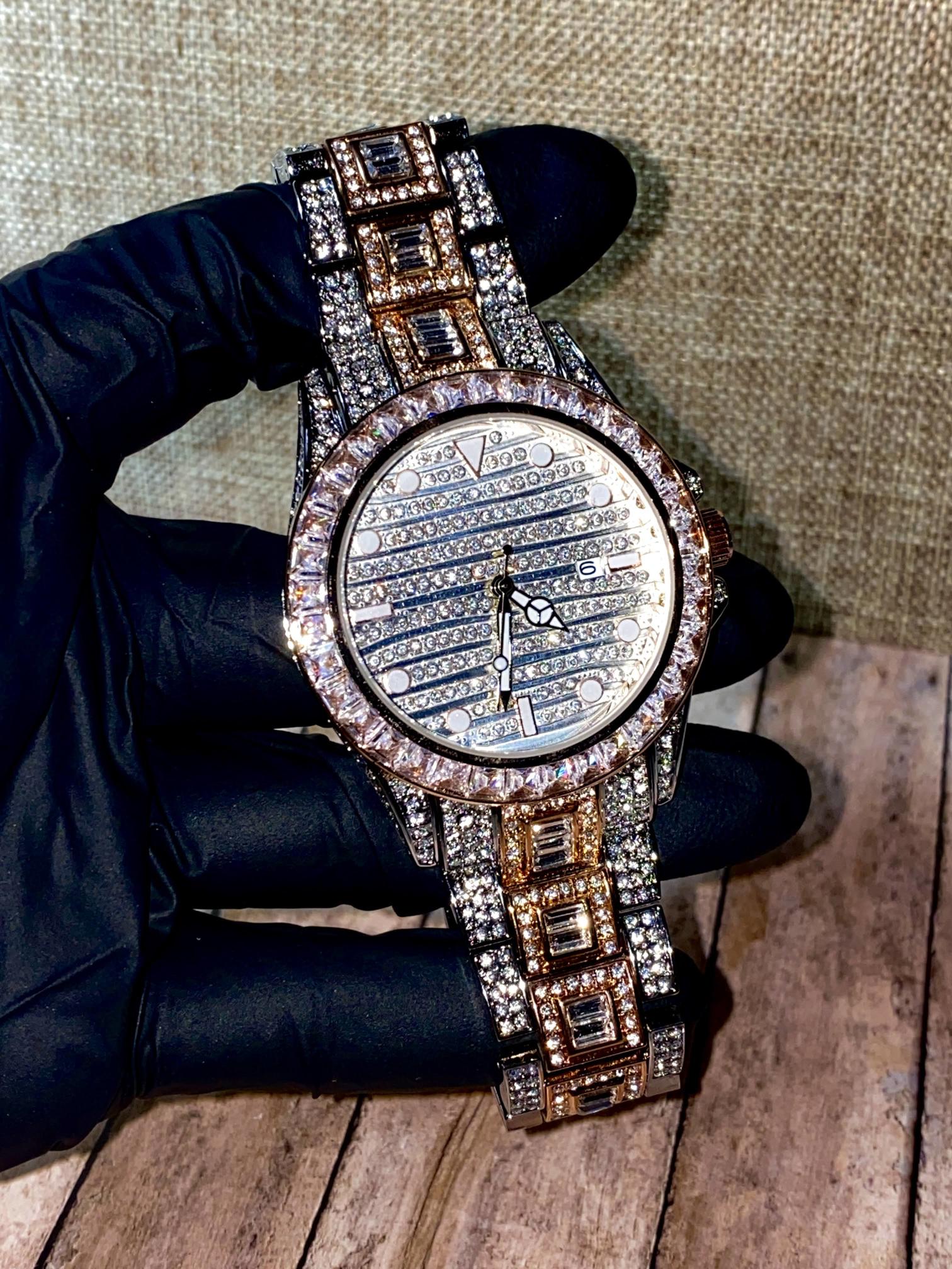Silver and gold men's women's watch with a diamond-studded bezel and rectangular stone accents on the band. The watch features a sleek white dial with black hands and a date display.