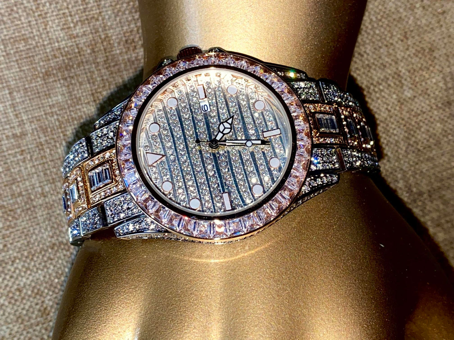 Silver and gold men's women's watch with a diamond-studded bezel and rectangular stone accents on the band. The watch features a sleek white dial with black hands and a date display.
