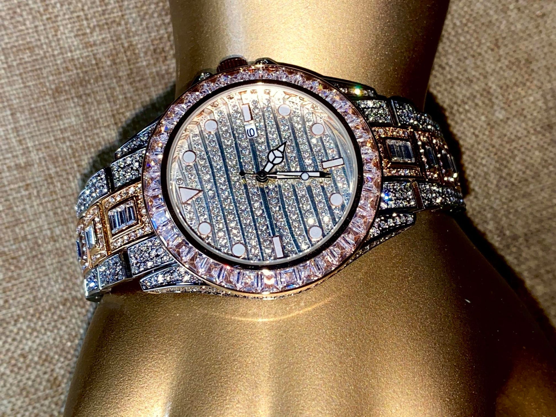 Silver and gold men's women's watch with a diamond-studded bezel and rectangular stone accents on the band. The watch features a sleek white dial with black hands and a date display.
