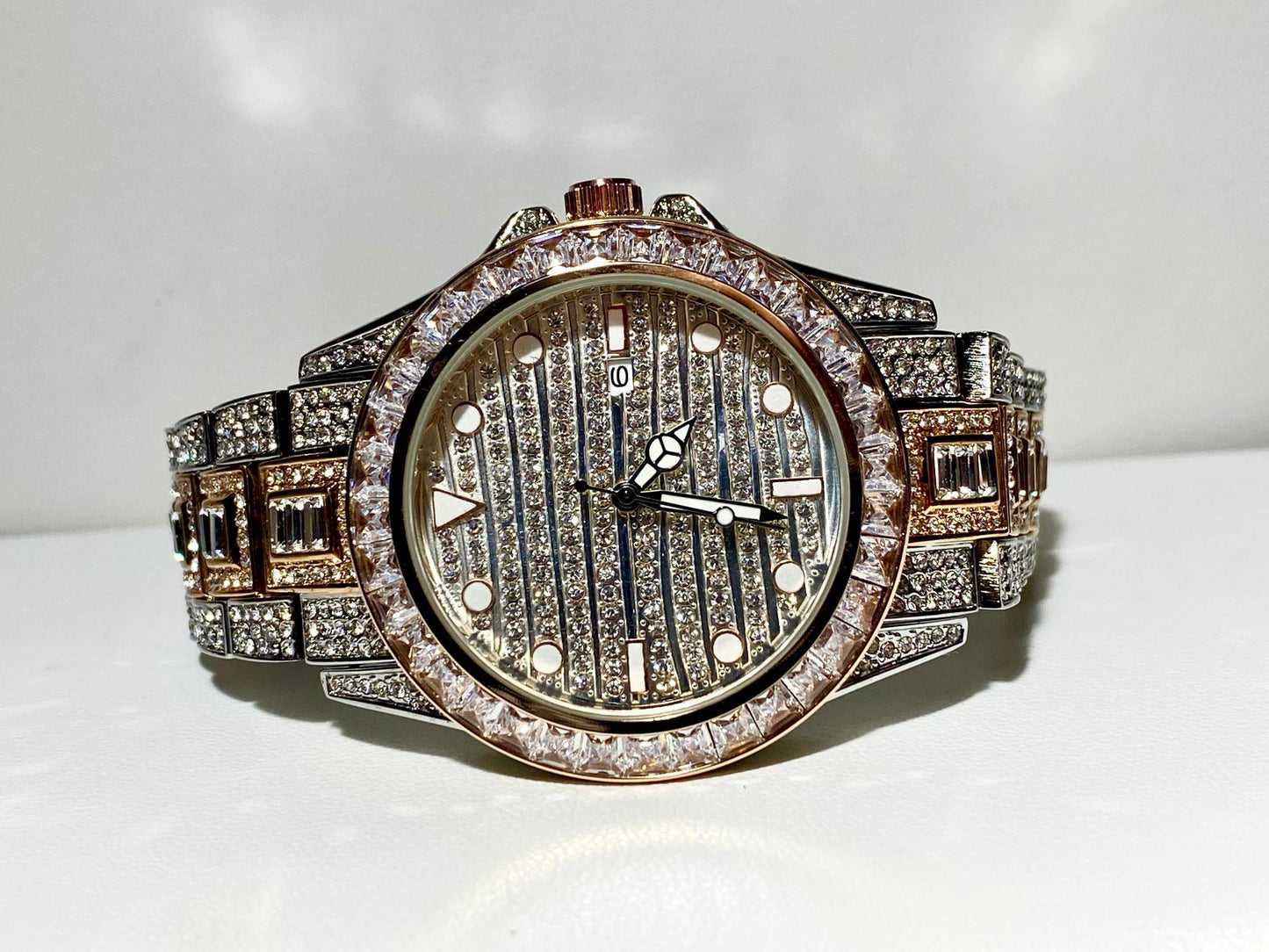 Silver and gold men's women's watch with a diamond-studded bezel and rectangular stone accents on the band. The watch features a sleek white dial with black hands and a date display.