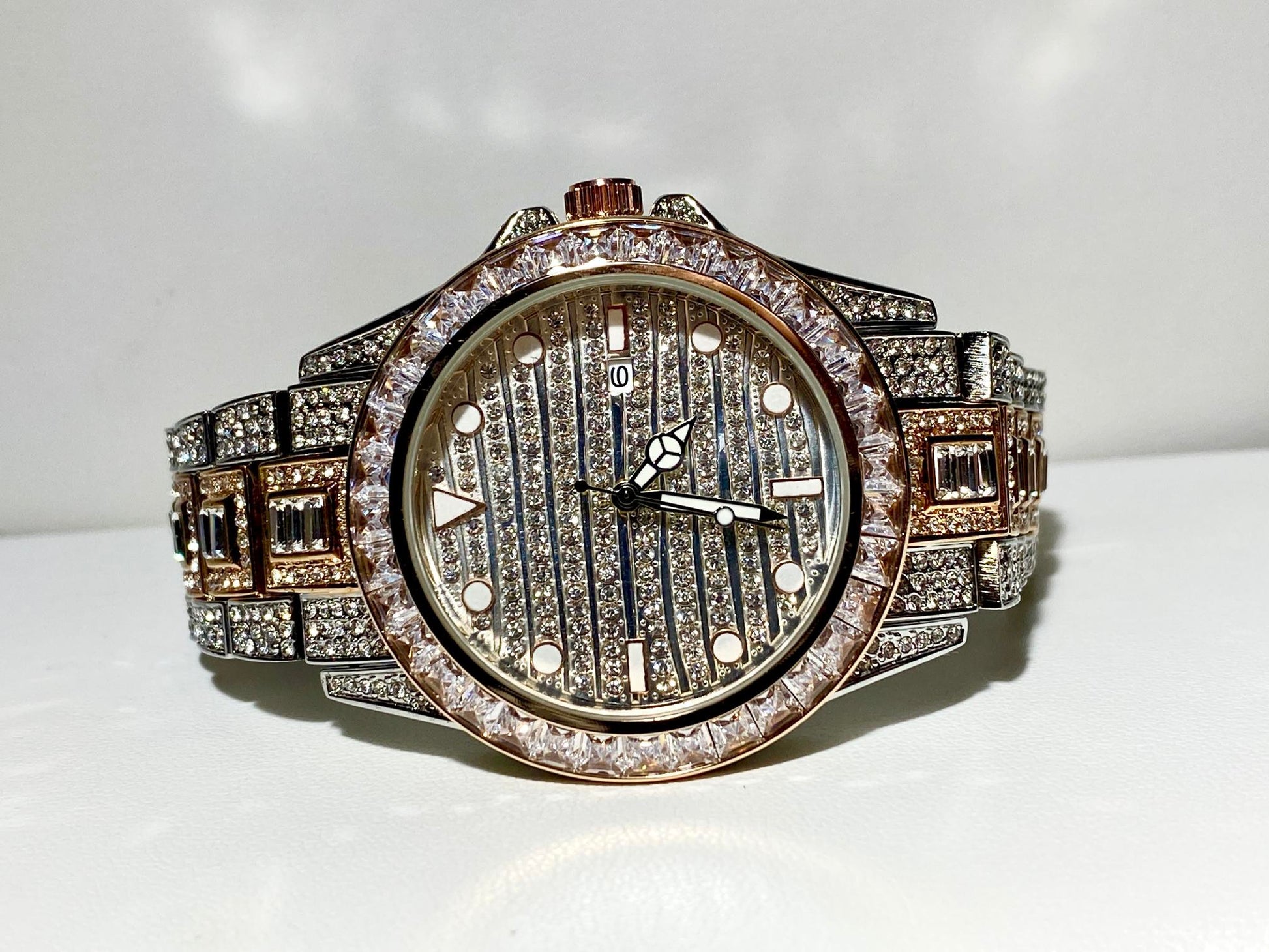 Silver and gold men's women's watch with a diamond-studded bezel and rectangular stone accents on the band. The watch features a sleek white dial with black hands and a date display.