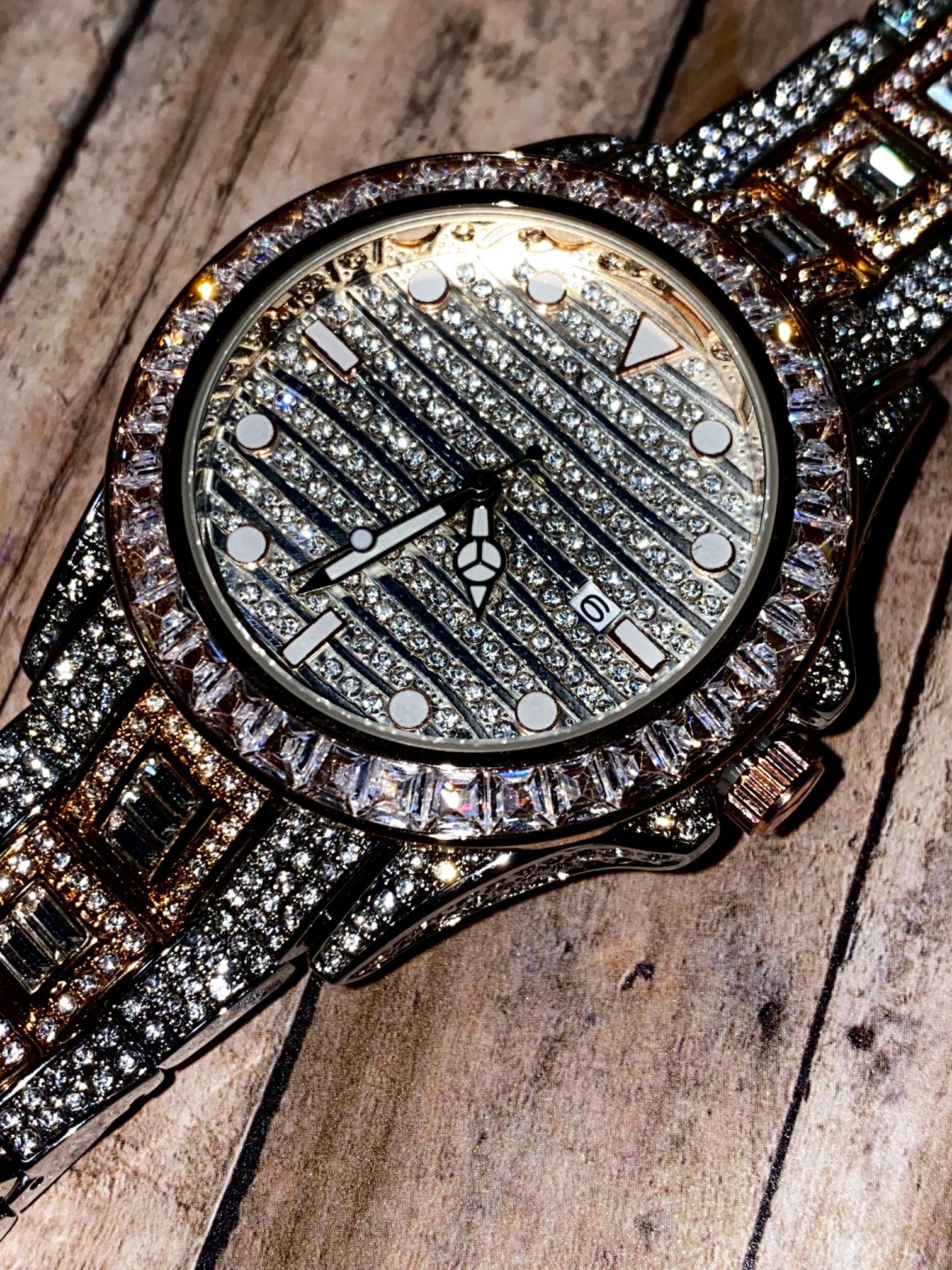 Silver and gold men's women's watch with a diamond-studded bezel and rectangular stone accents on the band. The watch features a sleek white dial with black hands and a date display.